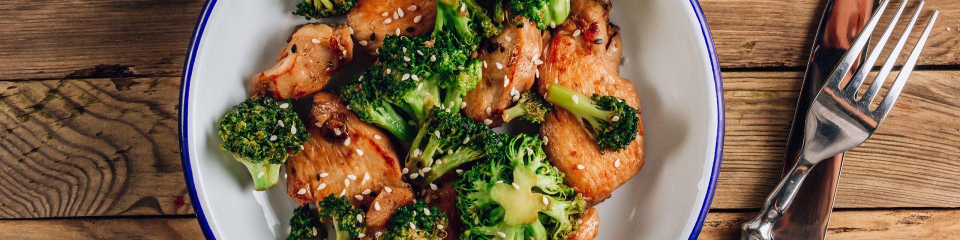 Chicken breasts and broccoli in soy sauce with sesame seeds for keto diet lunch. Rustic wooden background. Healthy food. Top view
